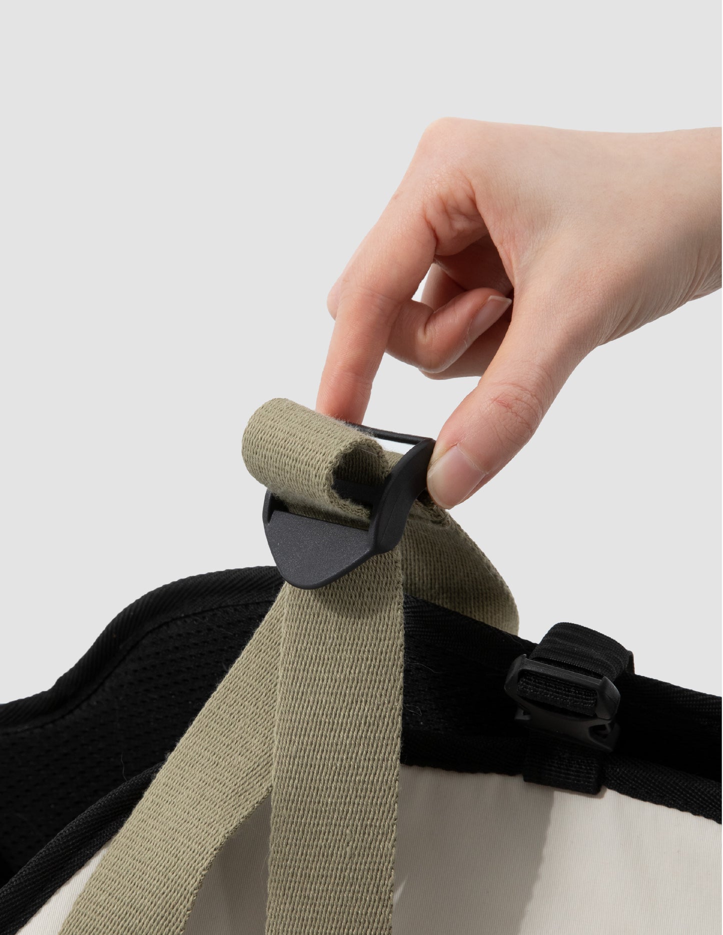 Hand adjusting a strap on a pet carrier with a plain background