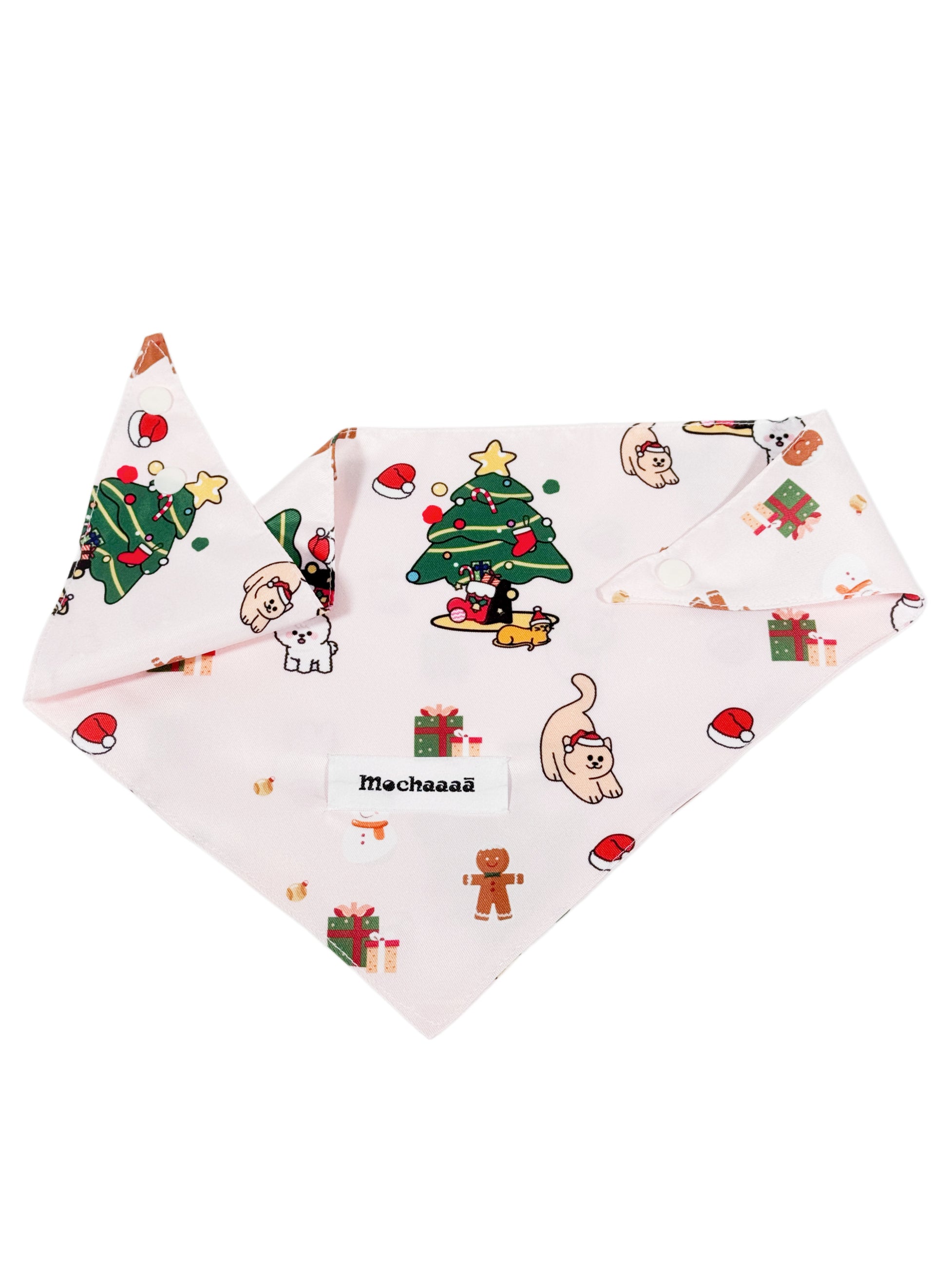 A light pink dog bandana featuring a festive Christmas print with cartoon cats, gingerbread men, Santa hats, and a Christmas tree. The bandana is displayed flat against a solid white background, with a white label in the center reading 'Mochaaaā'.
