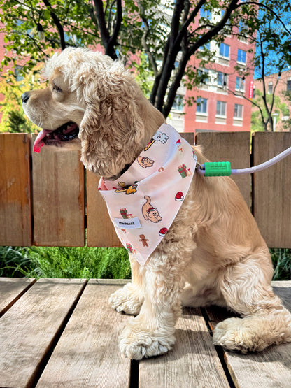 A light brown Cocker Spaniel dog sitting on a wooden deck outdoors, wearing a pink bandana with a cartoon monkey print and a green leash attached.