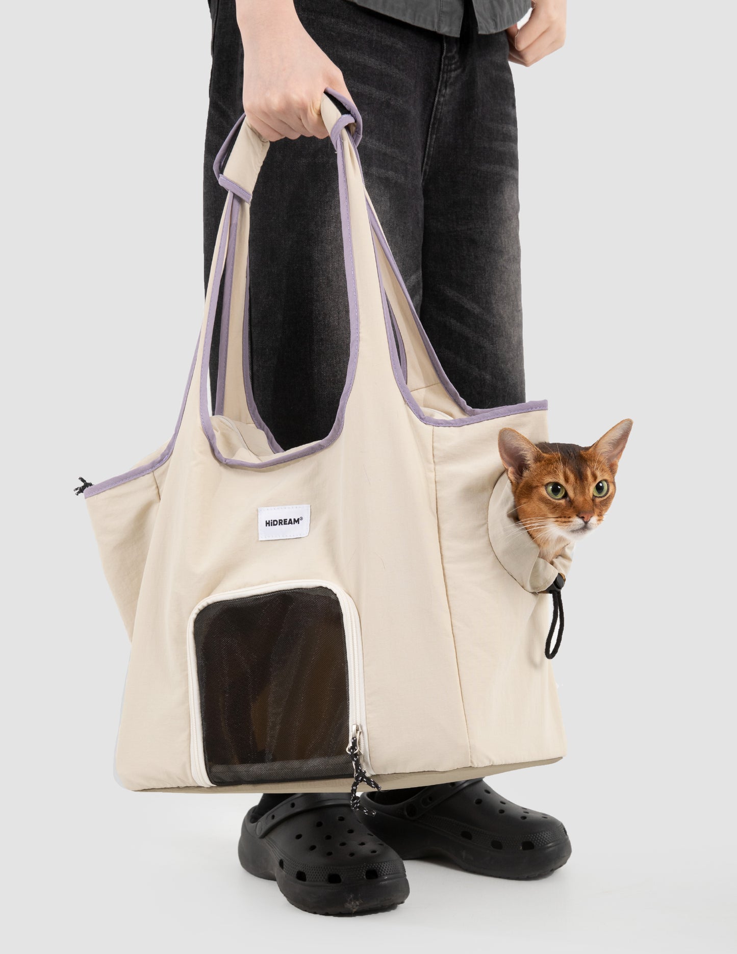 Person holding a beige pet carrier with a cat peeking out, on a white background