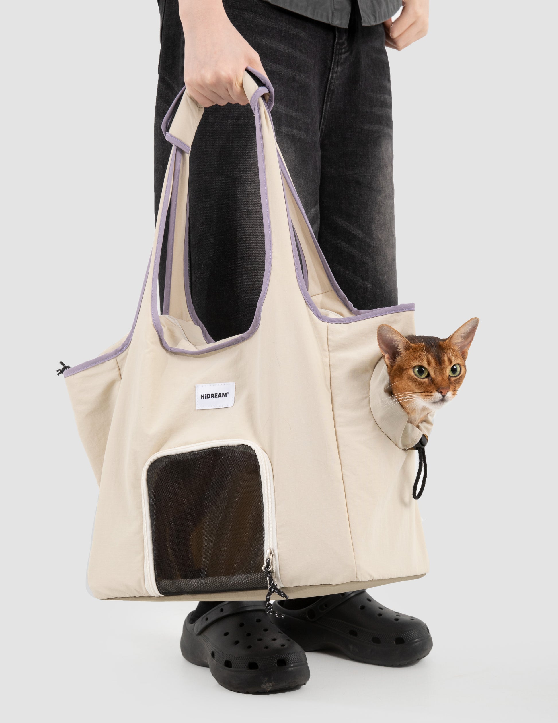 Person holding a beige pet carrier with a cat peeking out, on a white background