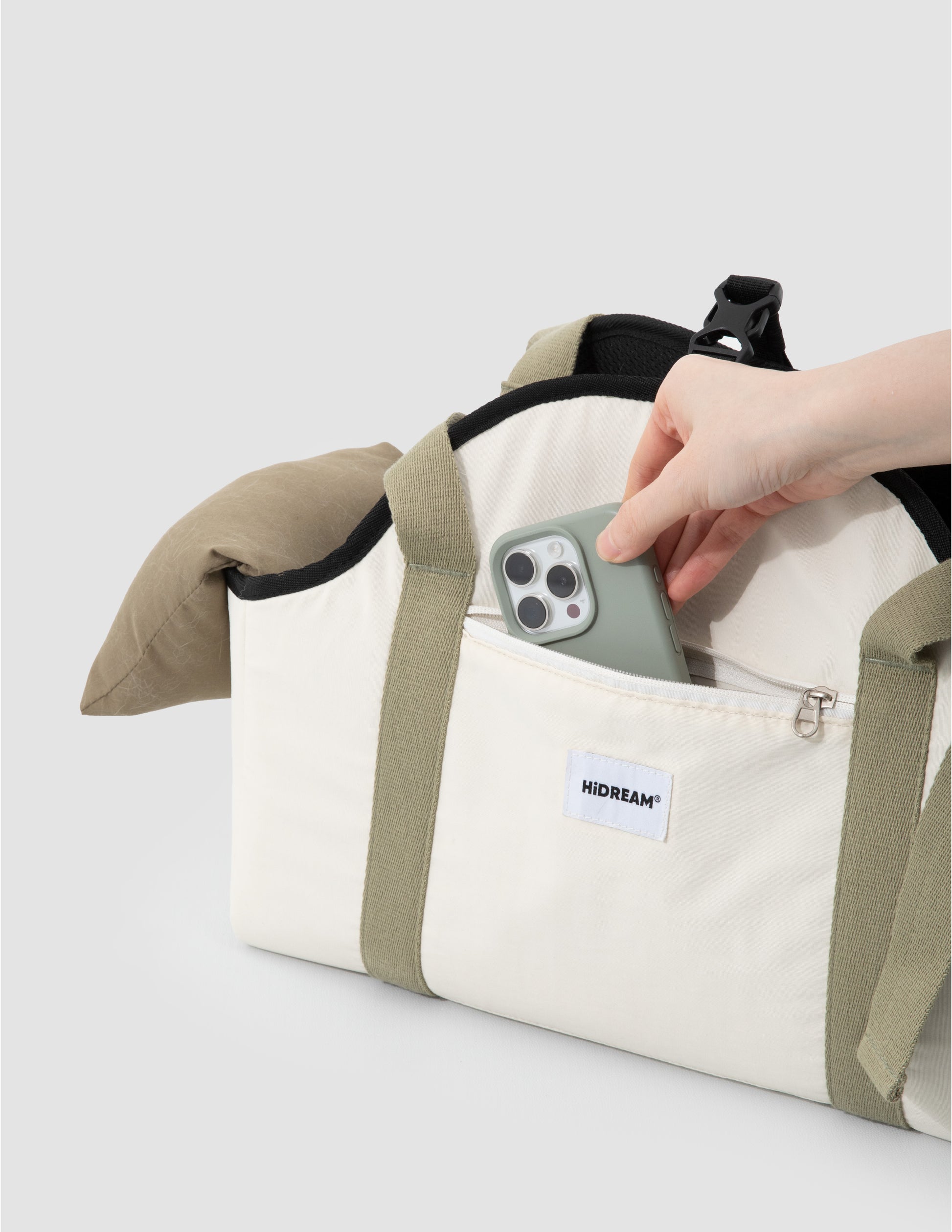 Hand holding a smartphone above a beige and green bag with 'HIDREAM' branding on a light gray background.