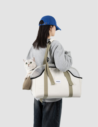 Person carrying a white bag with a gray cat inside, wearing a blue cap and gray hoodie on a light gray background