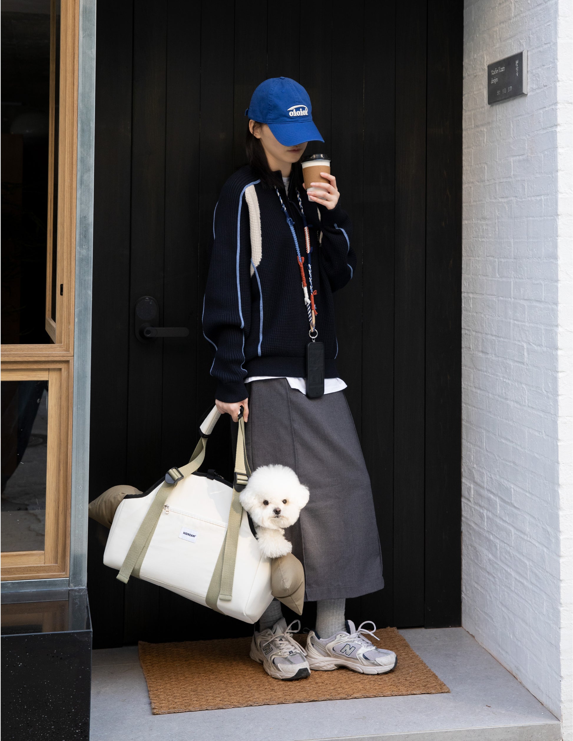 Person holding a small dog in a bag, standing outside a building.