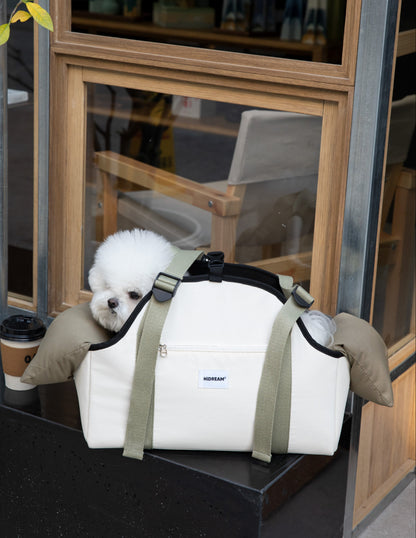 Small white dog in a white pet carrier with green straps, sitting on a black surface.
