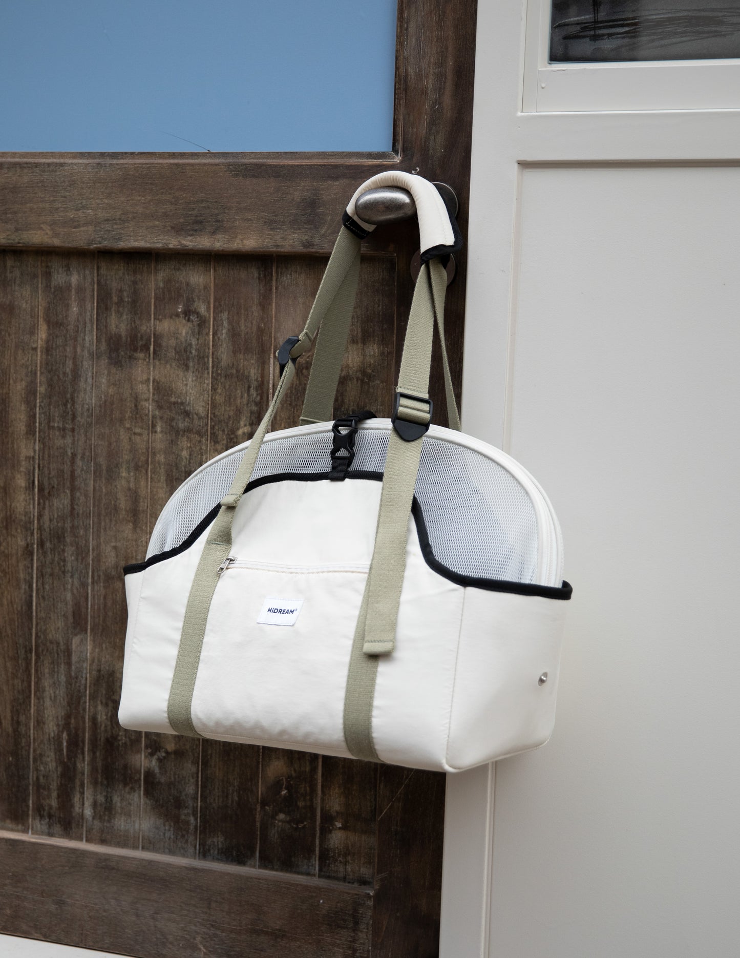 White pet carrier with green straps hanging on a wooden door.