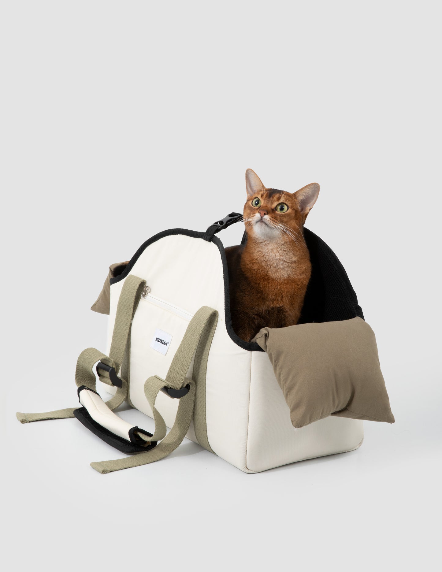 Cat sitting inside a white pet carrier with a brown pillow on a light gray background