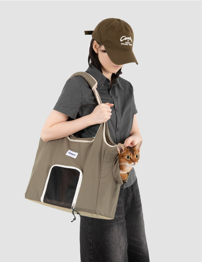 Olive green cat carrier tote bag with mesh window and side opening, worn over the shoulder while an orange cat looks out.