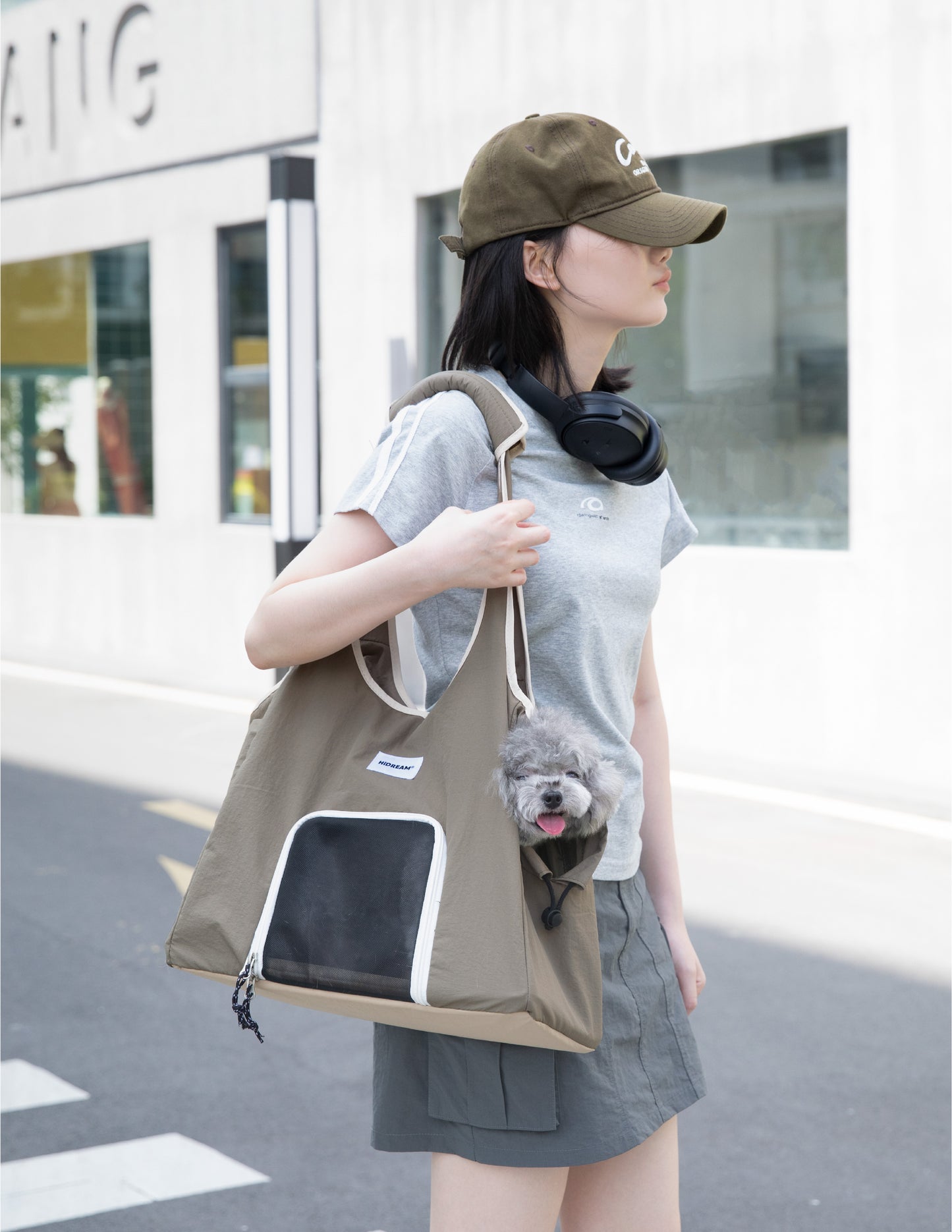 Olive green pet carrier tote bag with mesh front window, carried over the shoulder while a small gray dog peeks out from the side opening.
