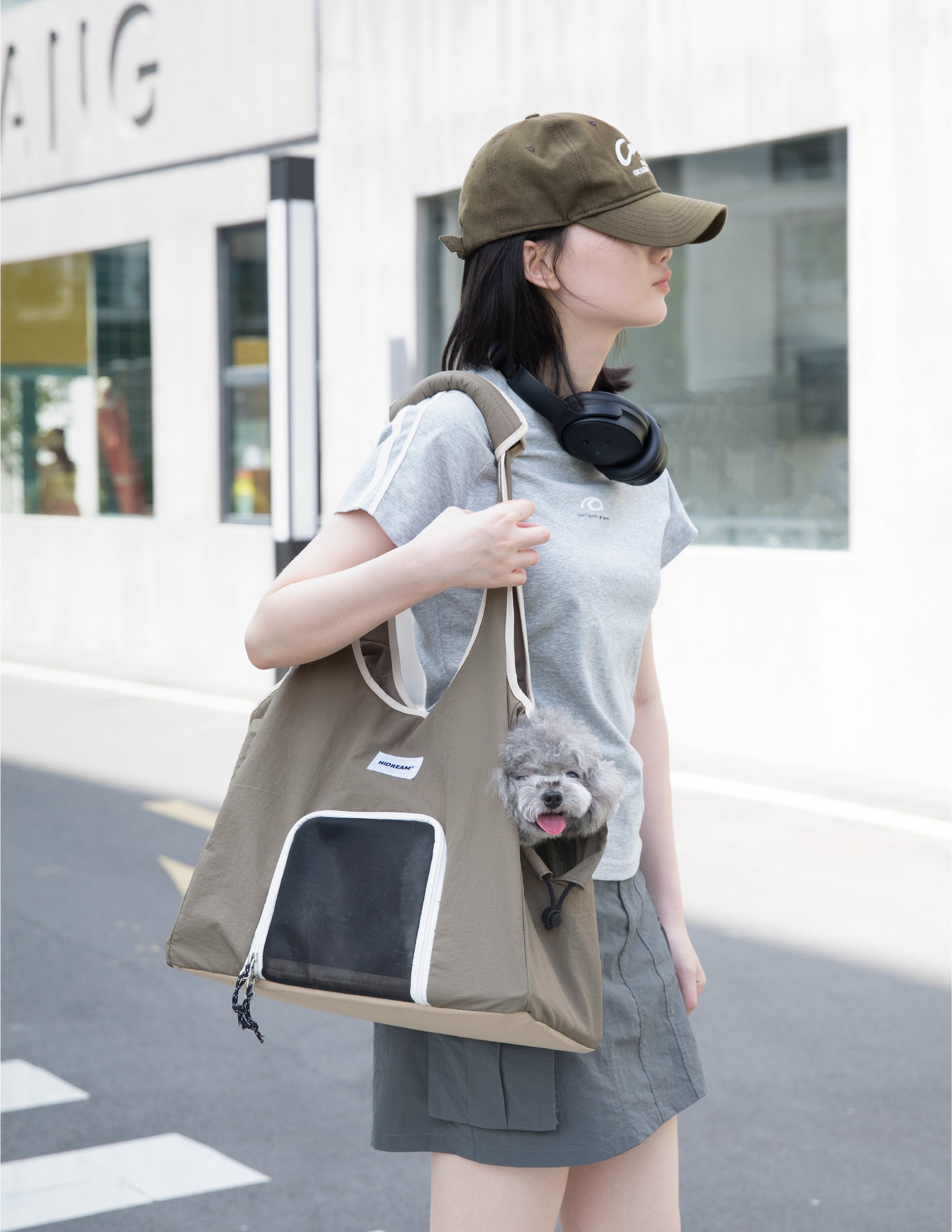 Olive green pet carrier tote bag with mesh front window, carried over the shoulder while a small gray dog peeks out from the side opening.