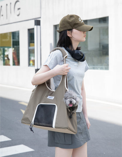 Olive green pet carrier tote bag with mesh front window, carried over the shoulder while a small gray dog peeks out from the side opening.