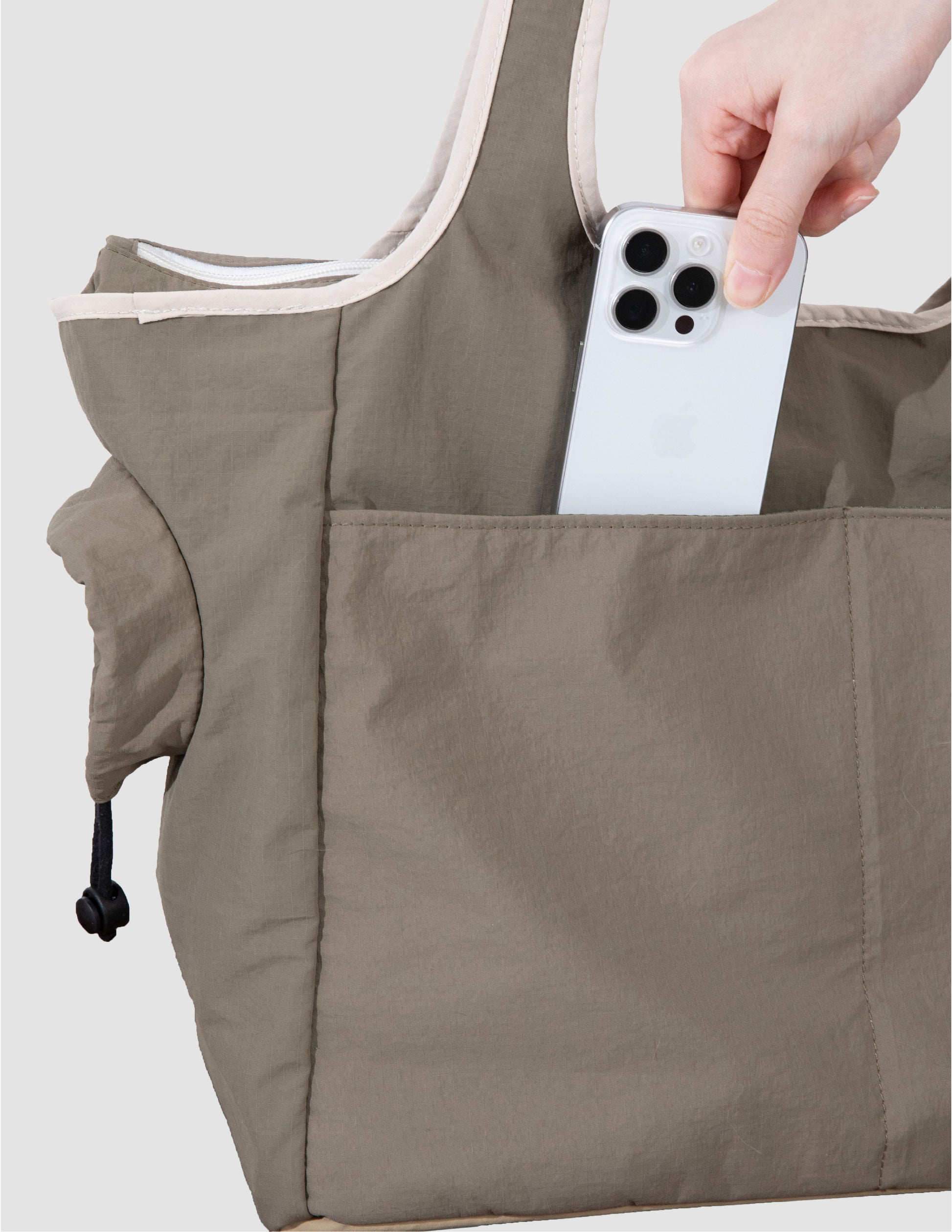 Person placing a phone into a pocket of a brown apron against a light background