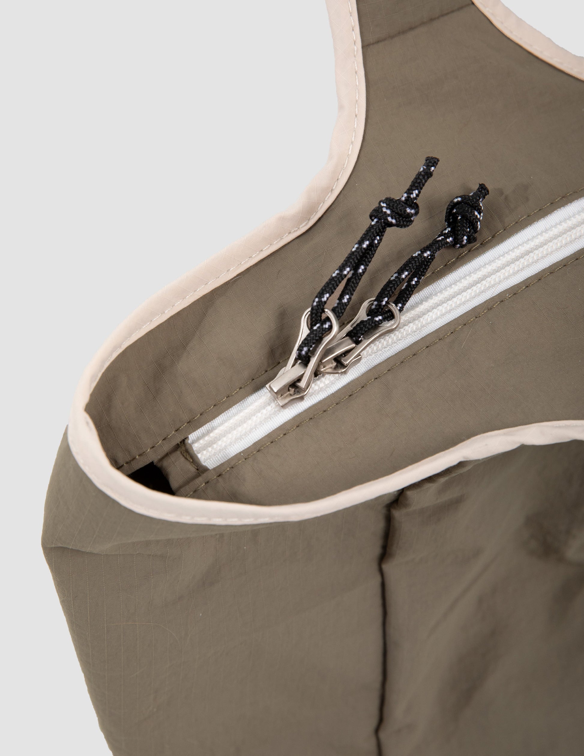 Close-up of a brown apron with a white zipper and black tie, on a light gray background.