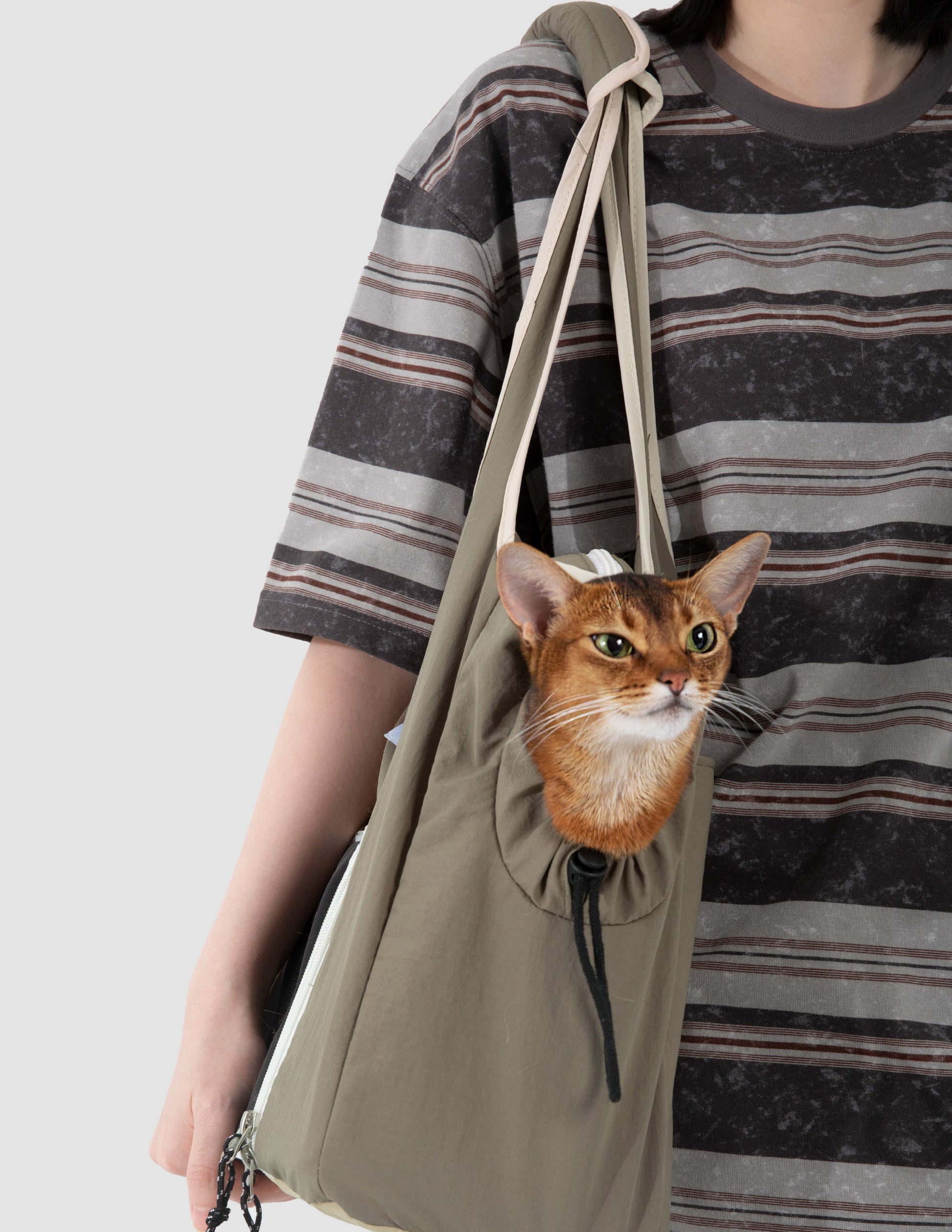 Person holding a khaki drawstring bag with a cat peeking out, wearing a striped shirt.