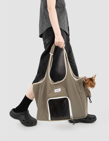 Olive green cat carrier tote bag with mesh window, carried by a person while an orange cat looks out from the side opening.