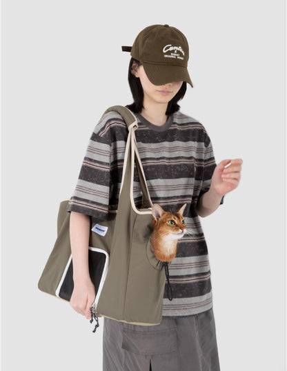 Person wearing a striped shirt and cap, holding a green tote bag with a cat peeking out.